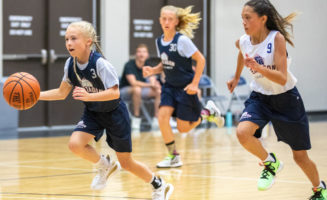 Two girls chase another young basketball player down the court.