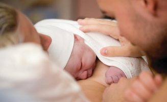 Newborn baby girl right after delivery, framed by mom and dad.