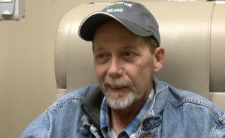 Mature man in a hat and jacket grins while seated for chemo treatment.