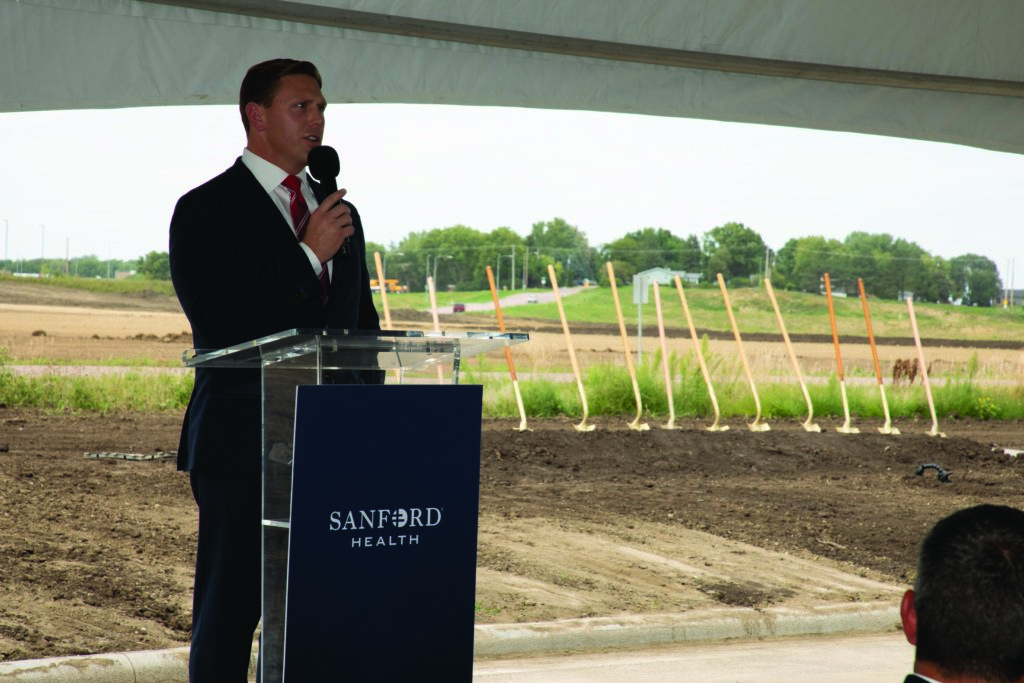 Sanford Health CEO speaks at a podium inside an event tent.