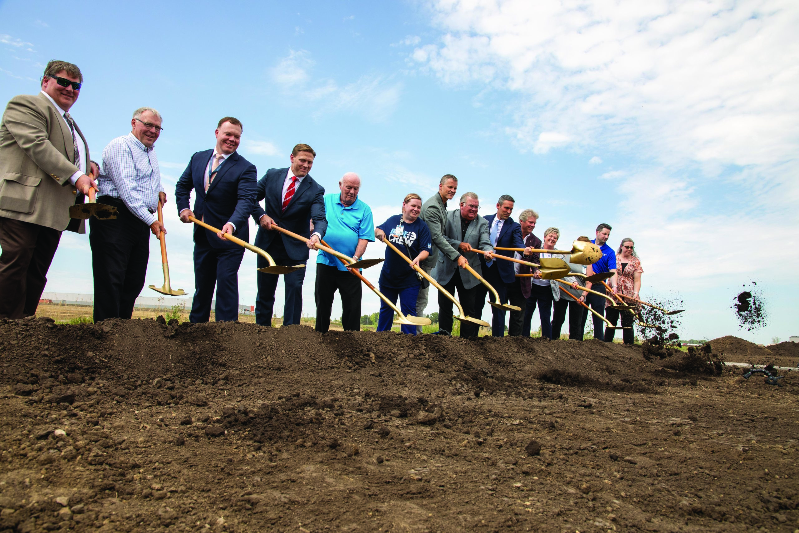 Sanford Health and community leaders line up with gold shovels, smiling and tossing scoops of dirt in the air.