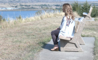 Woman in a sweater sits gazing at the river in Chamberlain, South Dakota.