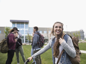 Smiling female college student with backpack on lawn on college campus