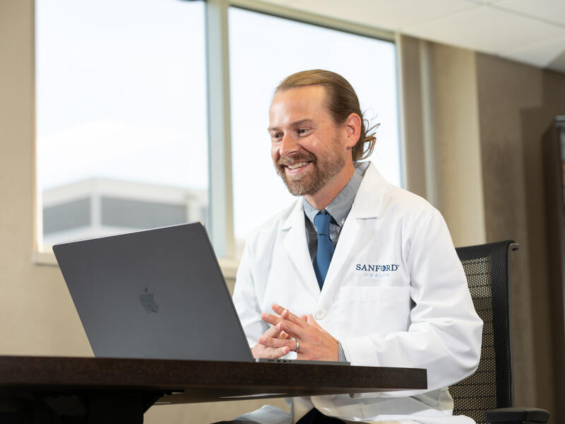 Dr. David Newman smiles while conducting a virtual care visit on his laptop.
