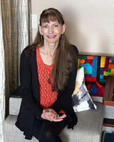 Candace Frohlich sits on a bench with a colorful quilt behind her.