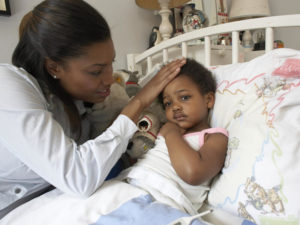 Mom puts her hand on her young child's forehead to check for fever while the child is sick in bed.