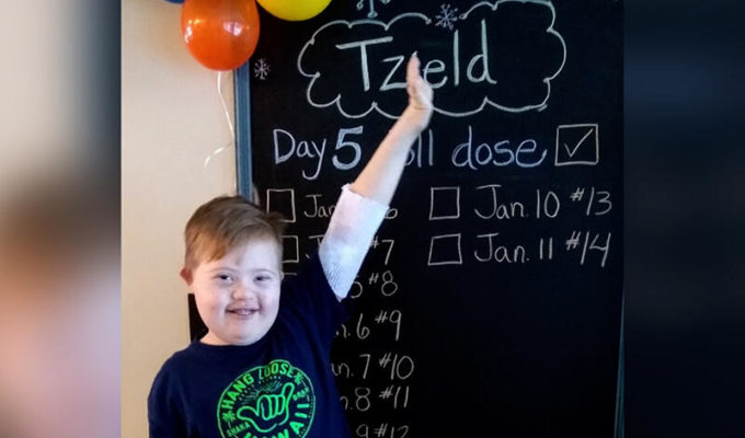 11-year-old boy raises his hand excitedly to show off his chalkboard countdown of Tzield diabetes treatments.