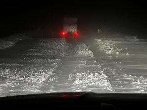 Brake lights on a semi-trailer light up the center of a snow-covered road.