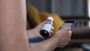 Closeup of patient holding prescription medicine bottle in one hand and smartphone in the other.