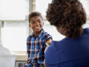 Happy child rolls up his sleeve for a nurse to bandage his upper arm after vaccination.