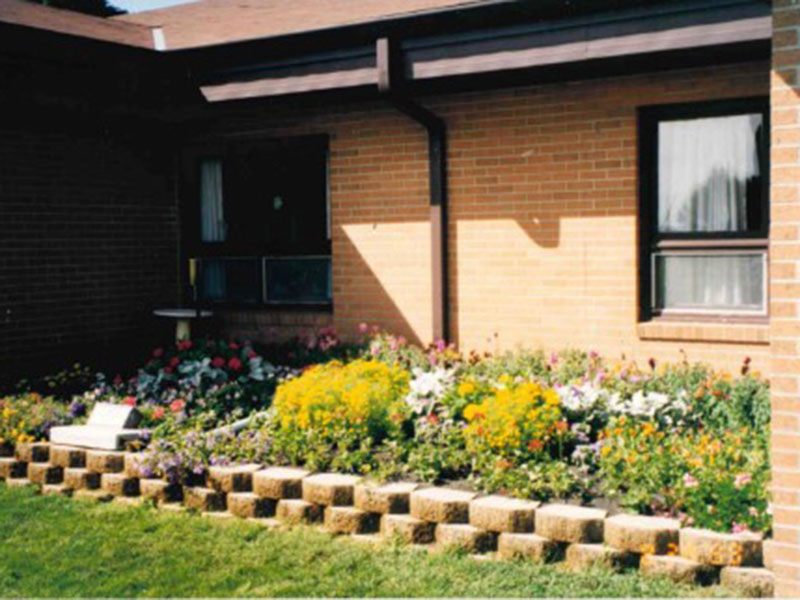A colorful flower bed creates a courtyard outside a brick senior living home.
