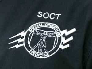 White logo embroidered on black cloth reads "SOCT: SPECIAL OPERATIONS MEDICINE" around an anatomical human figure in the middle of a circle with three lightning strikes behind it.