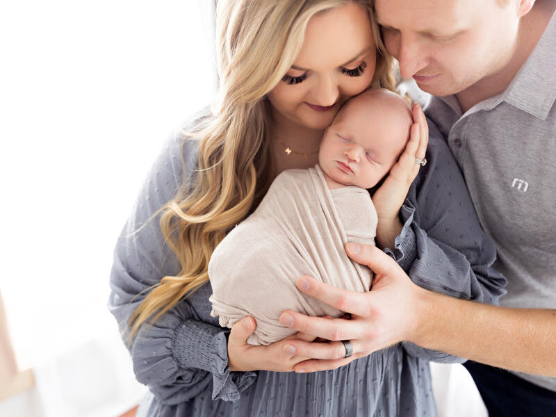 Kelsey and James Gibbons cuddle newborn baby swaddled in mom's arms.