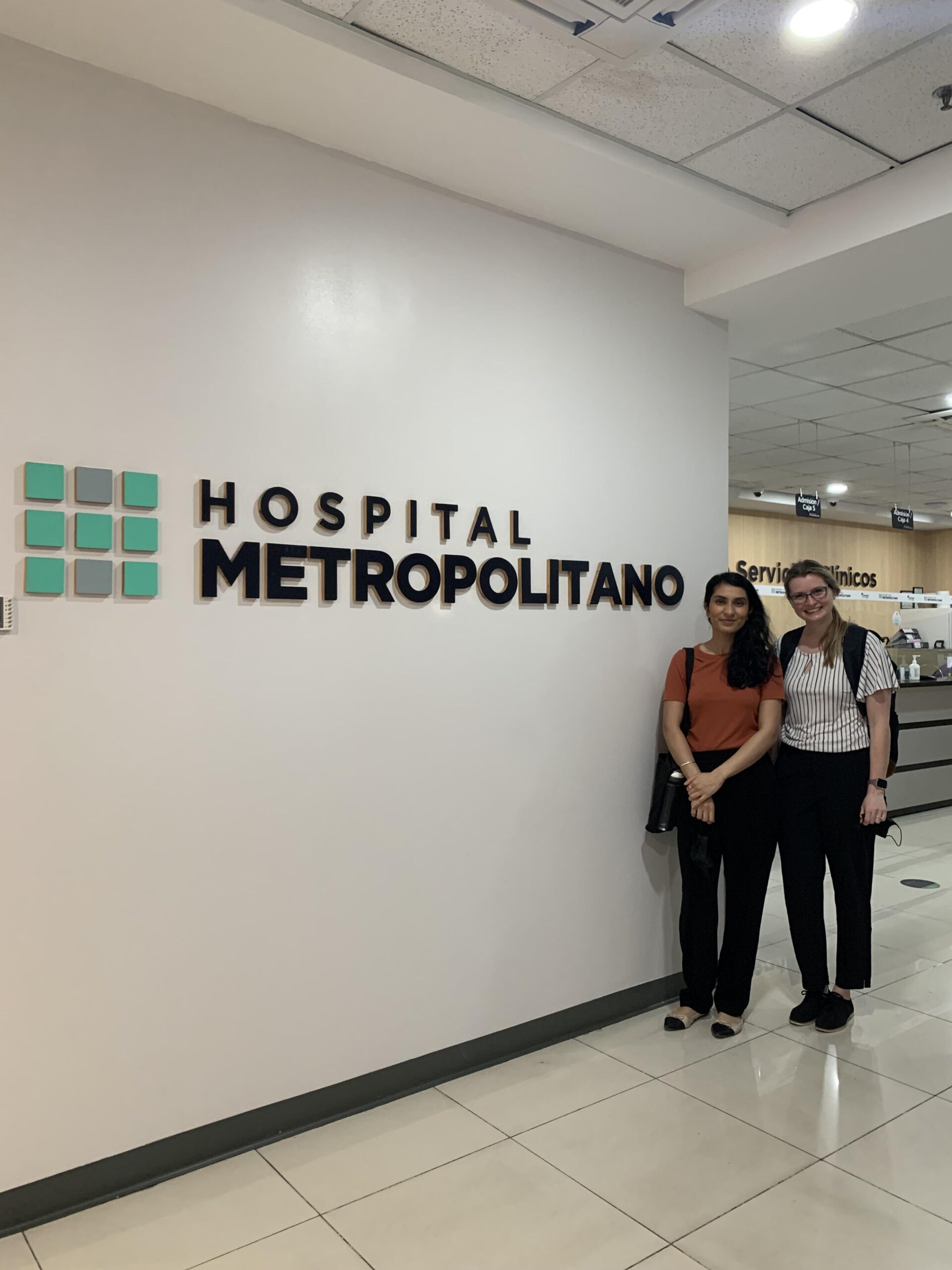 Two Sanford Health doctors stand next to an indoor sign for Hospital Metropolitano.