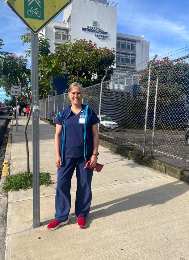 Sanford nurse smiles on sunny sidewalk outside a tall white building of Hospital Metropolitano.