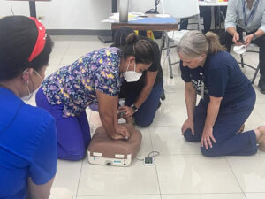 Nurses kneel on the floor to practice CPR on a medical mannequin torso.