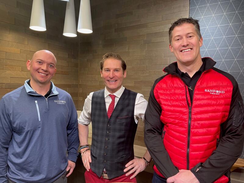Jared Antczak (in blue half-zip sweatshirt), Ken Hughes (in white shirt and black plaid vest), and Jeremy Cauwels (in red and black puffer jacket) smile in a podcast studio.