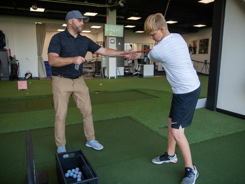 An instructor at Sanford Sports Academy helps a student with his golf swing.