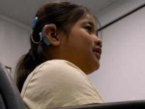 Profile of Kentaleen Akiuo in doctor's office with cochlear implant visible in her ear and hair.