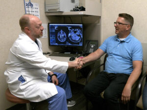 Dr. Adam Jackson shakes hands with surgical patient Scott Johnson, whose brain scans are on the computer screen between them.