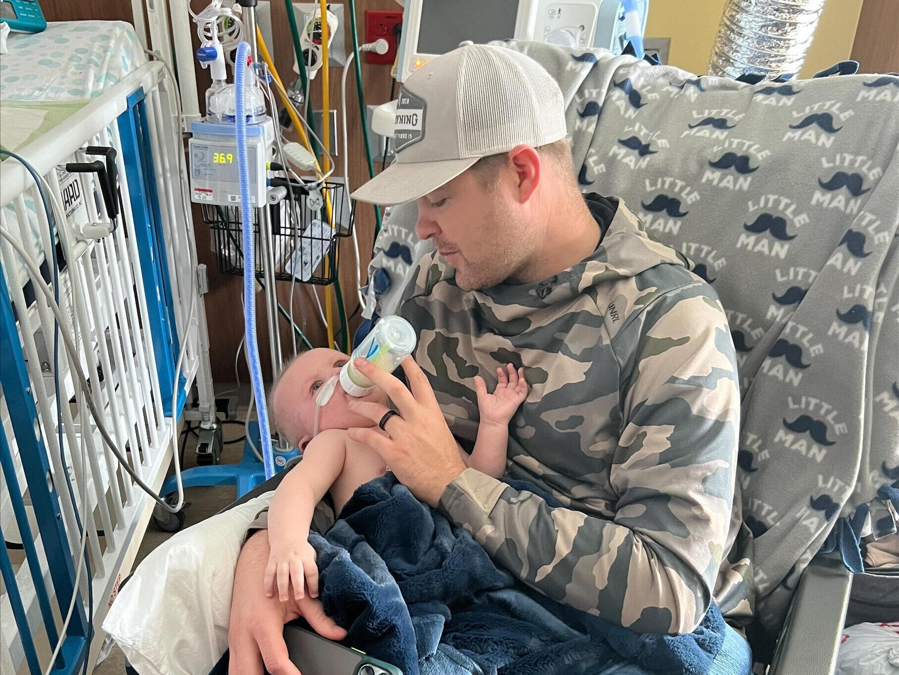 Dad holds his baby boy while feeding him a bottle in the hospital.
