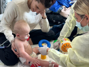 Mom, baby boy and health care workers play on the floor of the hospital room.