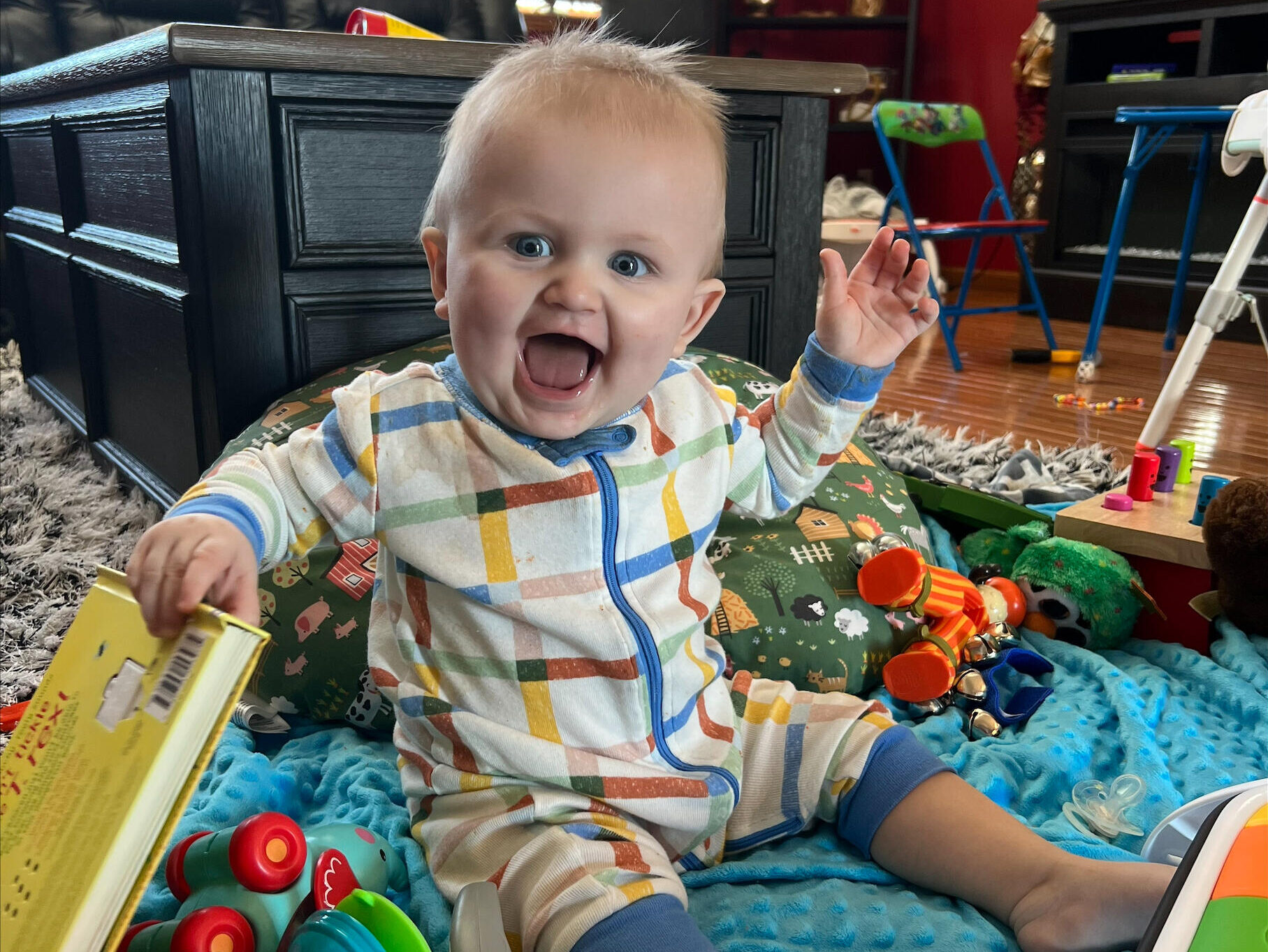 Happy baby boy plays with toys while sitting on the floor at home.
