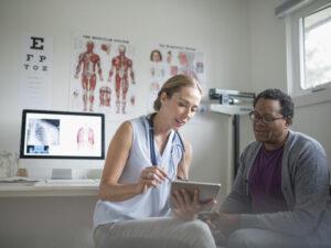 Female doctor with digital tablet talking with senior male patient in examination room.