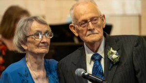 Two 96-year-olds in matching blue dress and suit and tie listen during their chapel wedding ceremony.