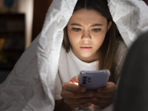 Teenager under a blanket frowns at her smartphone.