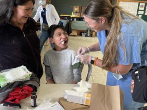 A mother and a young boy with cotton gauze in his mouth smile with a Sanford nurse at a clinic.