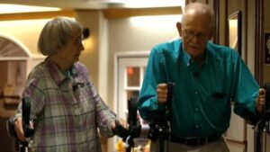 Older couple using walkers inside their nursing home.