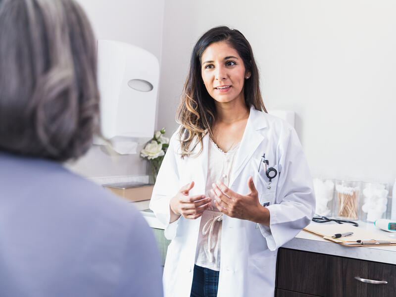 An unrecognizable female patient listens as a female doctor gives a diagnosis. The doctor is gesturing as she talks with the patient.
