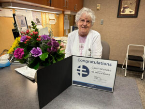Retiring nurse poses with flowers and a "congratulations" certificate from Sanford Health.