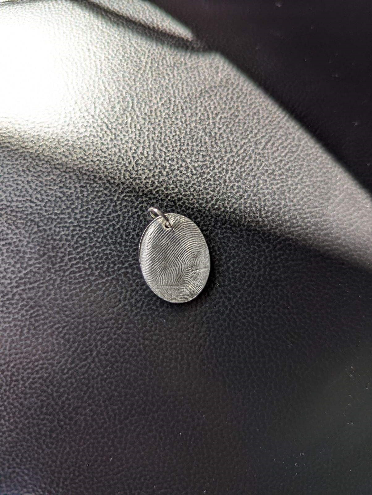Silver fingerprint charm on a dark background.