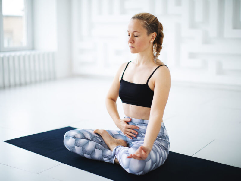 woman sitting, with legs crossed, on a yoga mat
