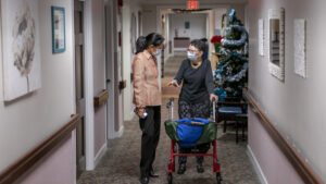 Screenshot from Politico. A caregiver and a woman using a walker in the hallway of a nursing home.