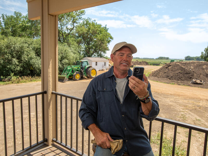 Farmer on his front porch talks on his smartphone.