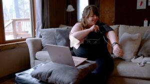 Happy pregnant woman uses a blood pressure cuff in front of an open laptop computer.