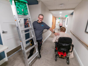 A man with a ladder pats the shoulder of a woman in a wheelchair.