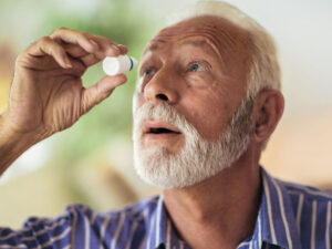Older man putting in eye drops for eye health, cataract surgery.