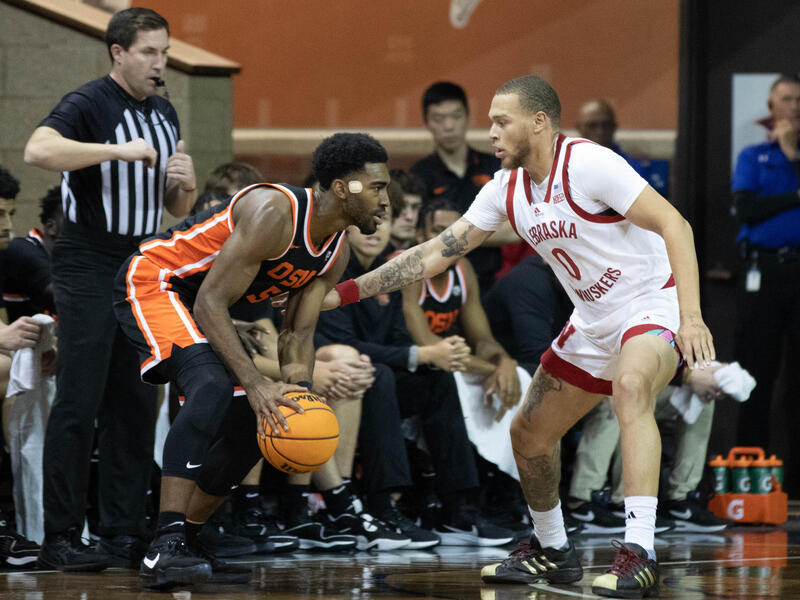 A referee gets ready to blow his whistle behind two college basketball players.