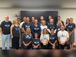 Sanford Health workers pose in matching blue and white T-shirts that display a Wonder Woman logo modified with a cancer awareness ribbon and the word "BATTLEMODE."