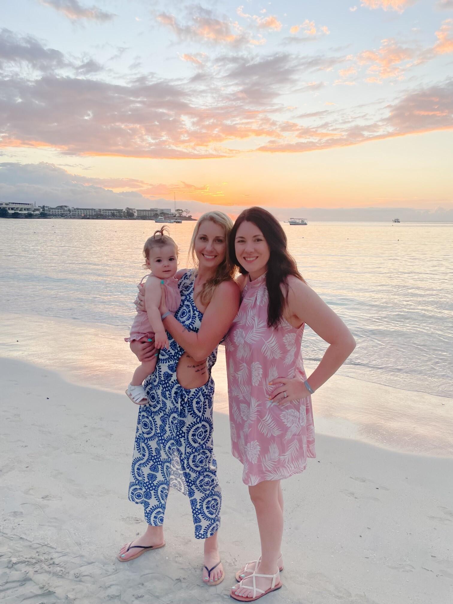 Two women hold their baby on the beach at sunset.