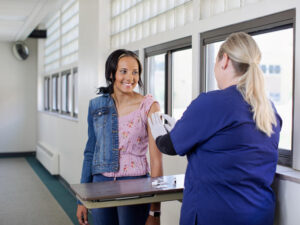 Teen girl smiles at nurse who places a bandage on her upper arm after vaccination.
