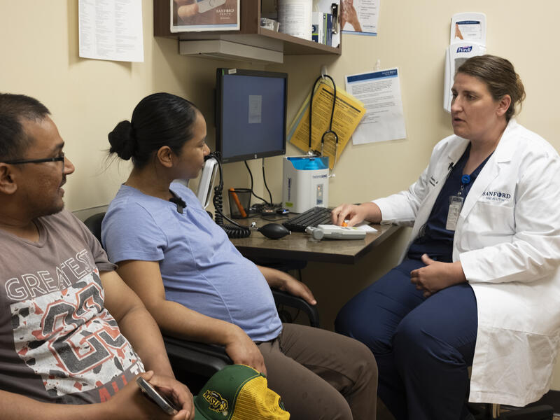 Doctor meets with a pregnant woman and husband in an exam room.