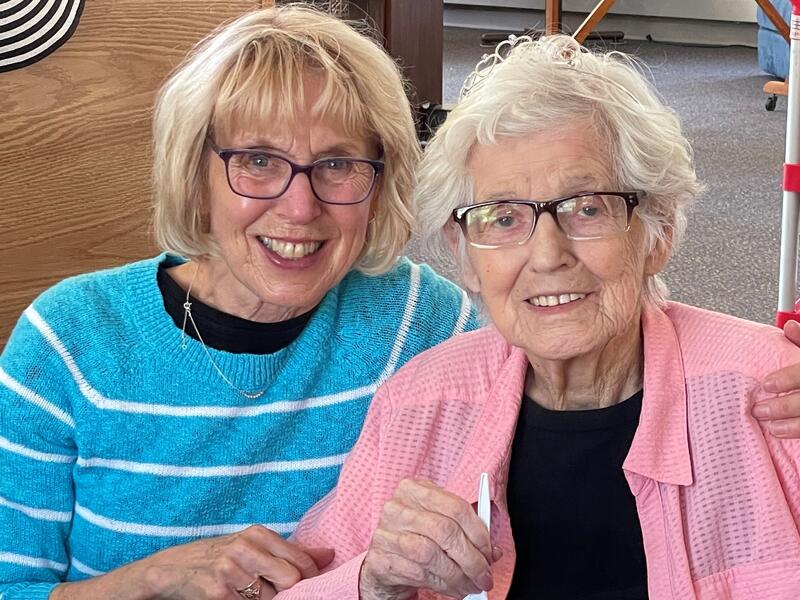 Middle-aged daughter and senior mother smile in their home.