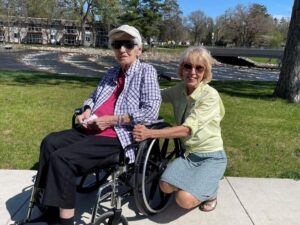 Mother and daughter on a sunny walkway by a river. The mother is using a wheelchair.