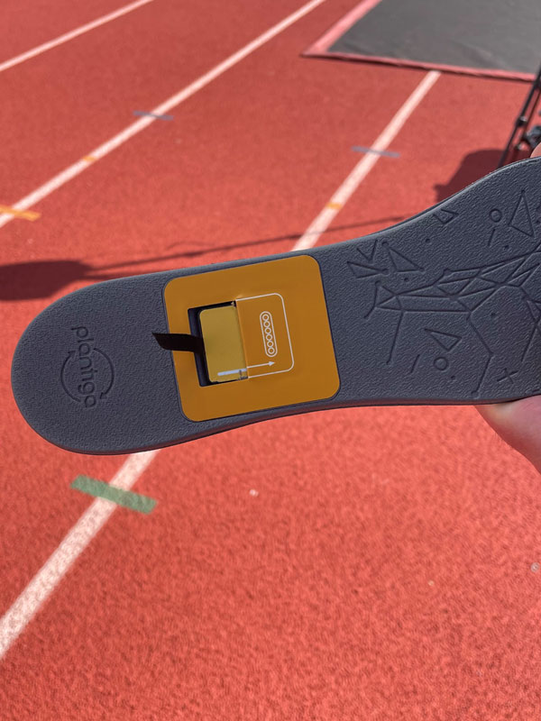 Shoe insole held above a running track. The insole has a GPS data card inserted in the middle.