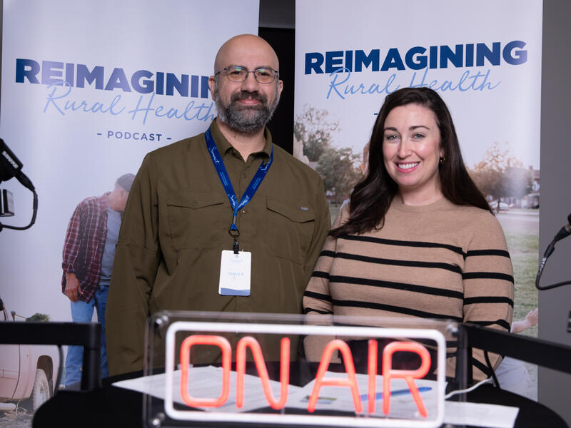 man stands next to woman behind on-air sign